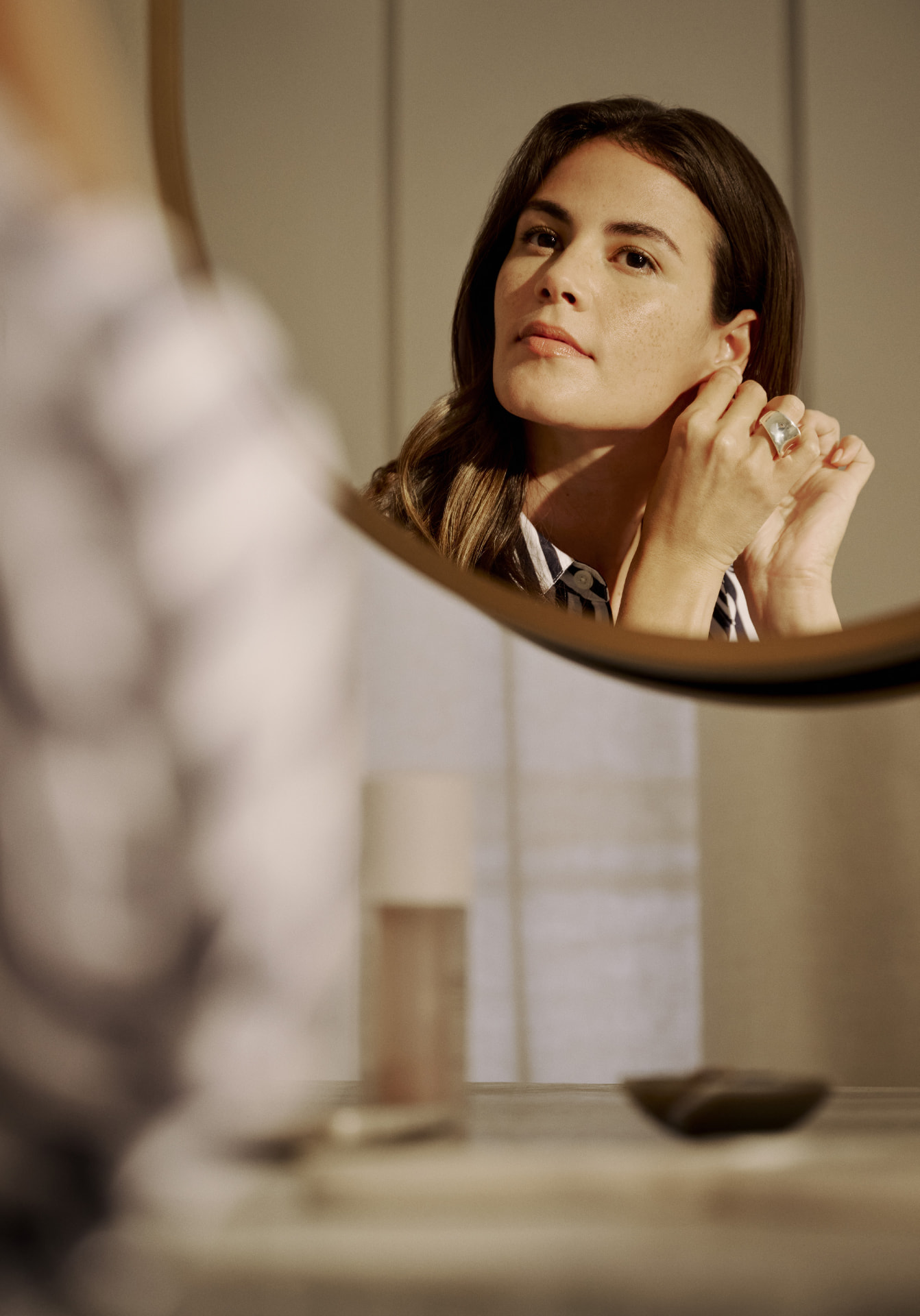 Woman fastening an earring, reflected in a round Kallista mirror