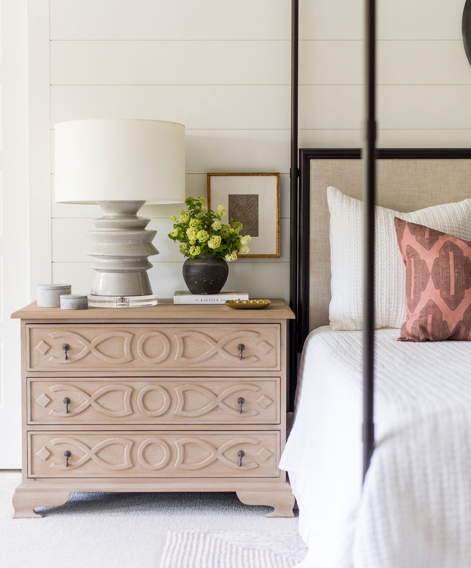 A carved oak chest beside a canopy bed with a sculptural ceramic lamp