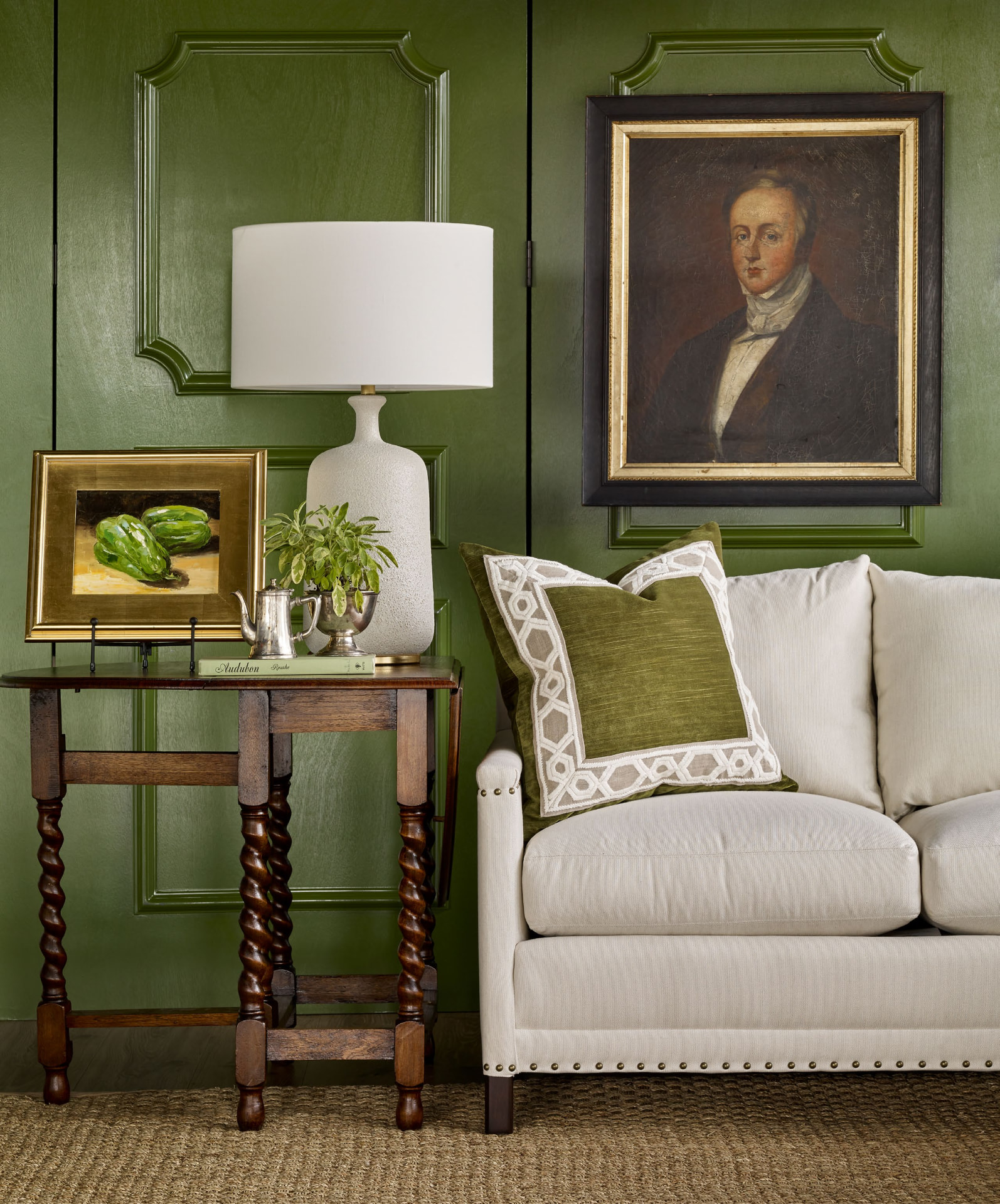 Green lacquered paneled room with antique portrait, lamp and velvet pillow