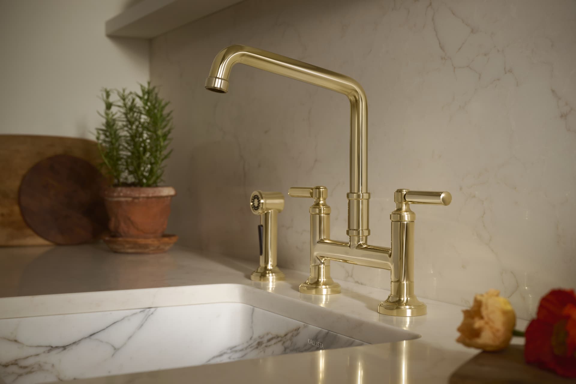 Polished brass bridge faucet with side spray against a marble backsplash