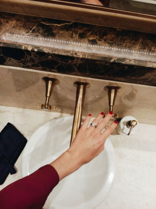Hand reaching for a brass wall-mount faucet over a white basin