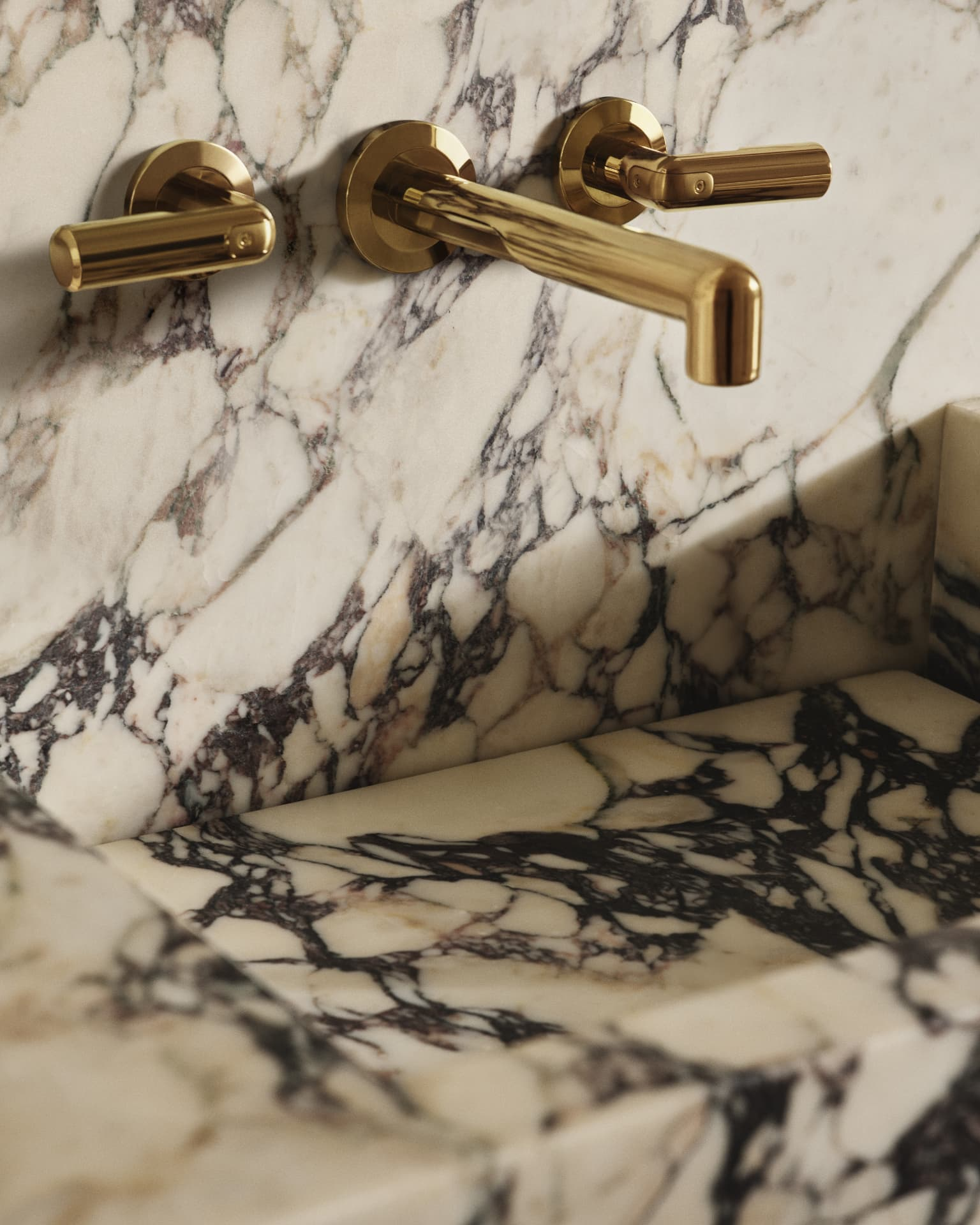Polished brass Kallista wall-mount faucet set into richly veined marble