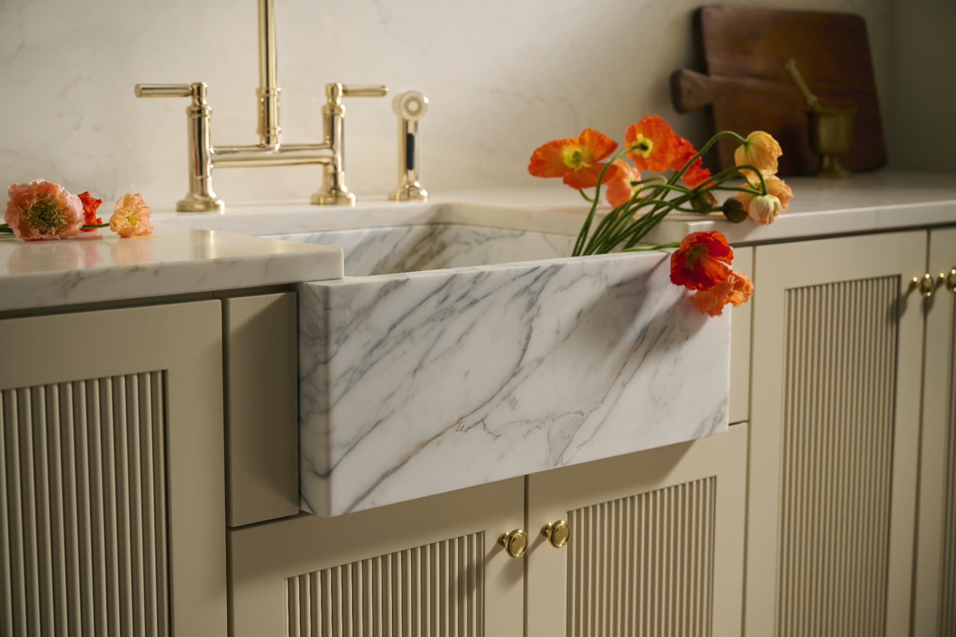 Marble apron-front sink with brass bridge faucet and poppies on fluted cabinetry