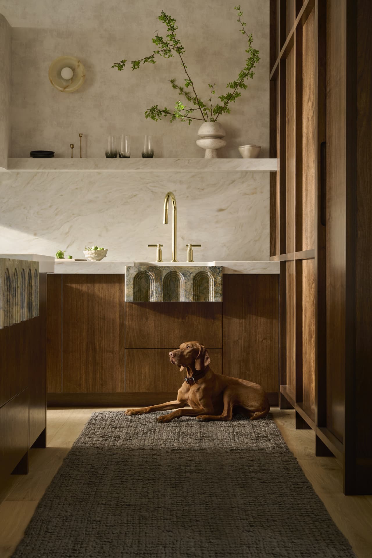 Warm walnut kitchen with marble island and a Vizsla dog resting on a woven runner