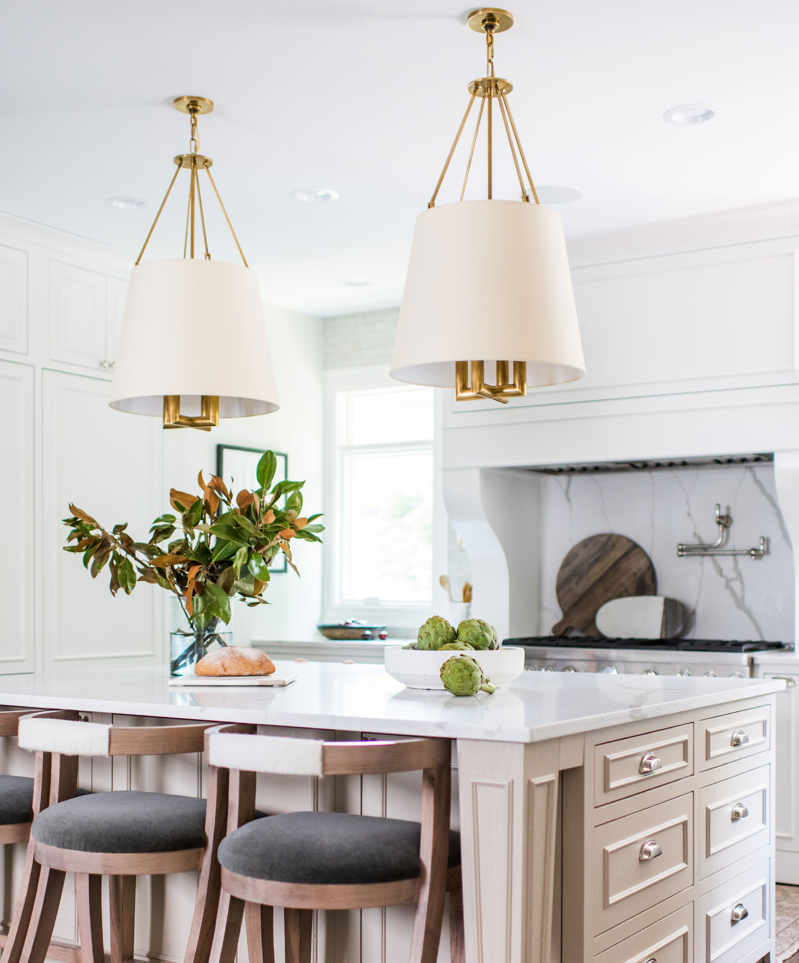 A bright white kitchen with brass pendant lights over a marble island