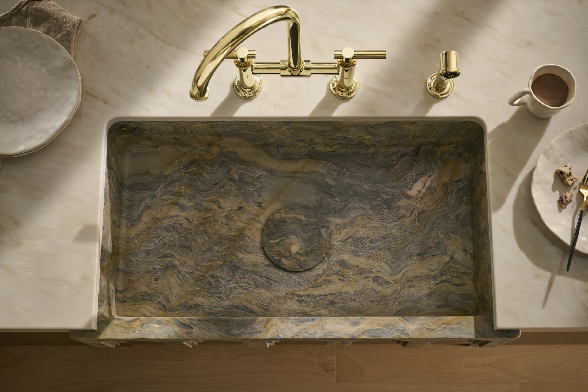 Overhead view of a stone sink with brass bridge faucet and morning coffee