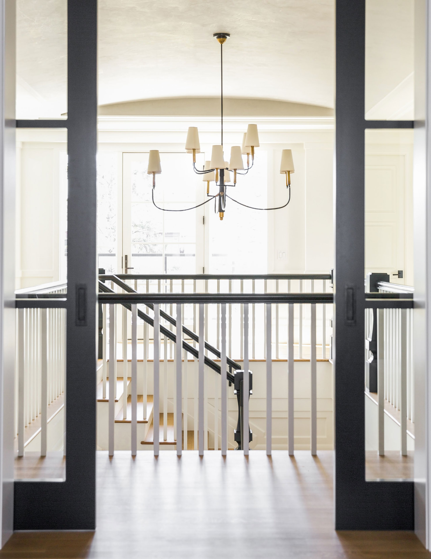 Chandelier above a white staircase seen through dark pocket doors