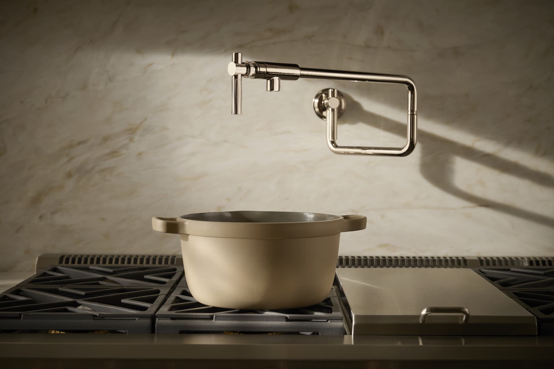 Polished nickel wall-mount pot filler above a range with a stoneware pot