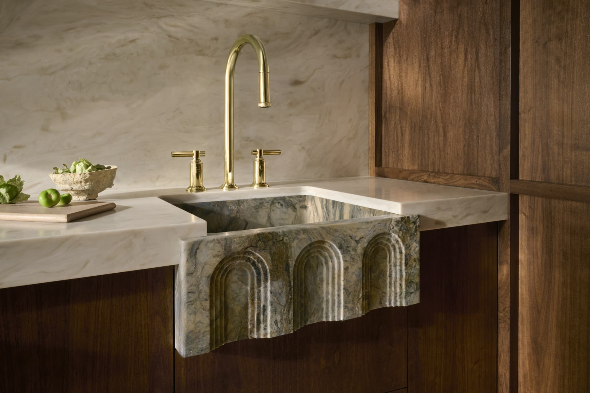 Fluted stone farmhouse sink set into marble against walnut cabinetry
